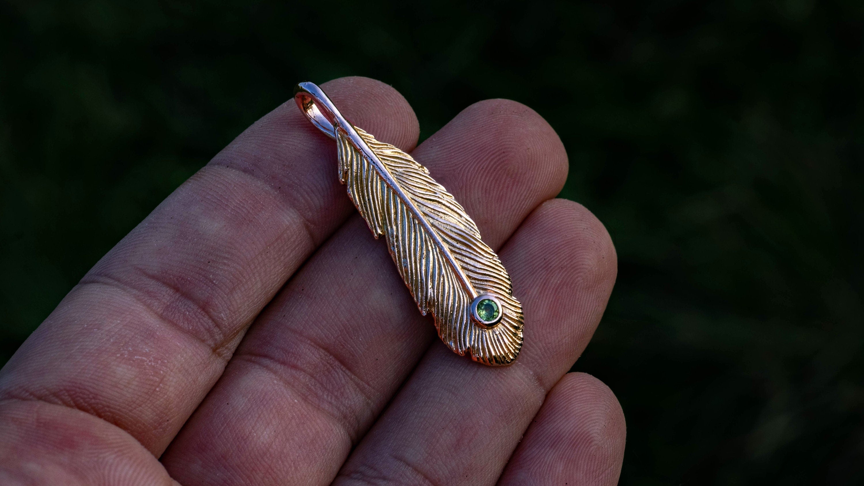 Handmade gold peacock feather necklace on dark background
