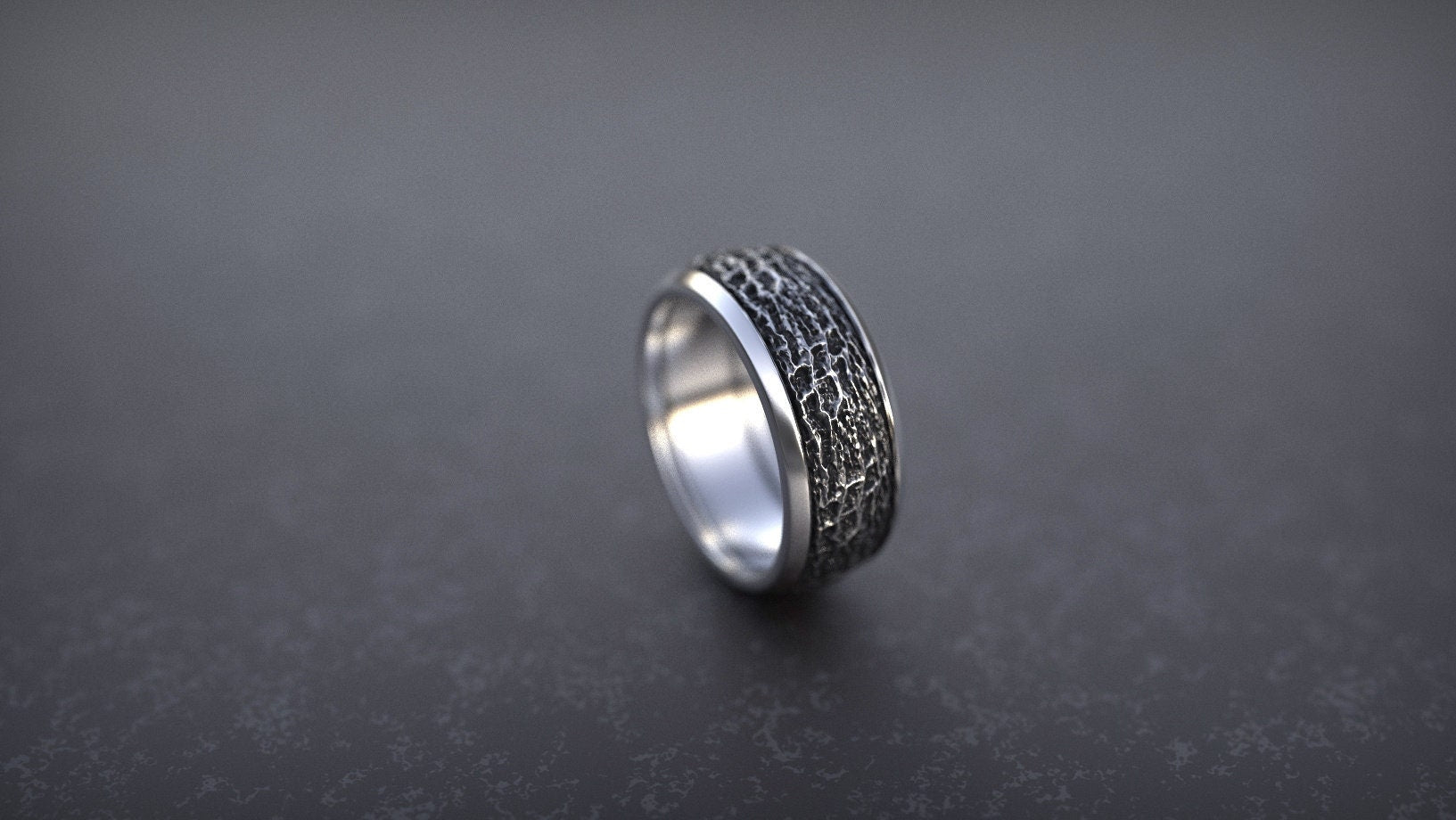 Silver ring with a tree bark pattern carved around its surface, resting on a textured grey  background,